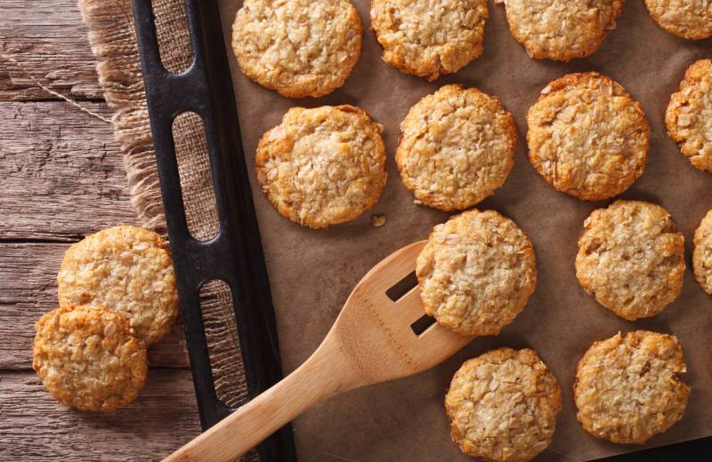 A baking tray filled with anzac biscuits, with a wooden spoon
